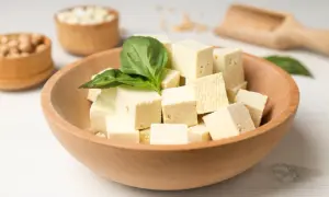 Kostki tofu w drewnianej misce, ozdobione listkiem bazylii. Czy tofu można jeść na surowo? Tak, to świetna baza do sałatek!