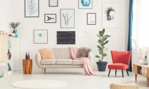 Sofa w kolorze ecru, jaki to kolor? Delikatny, przytulny, idealny do salonu. Obok niej czerwony fotel i mnóstwo obrazów na ścianie.