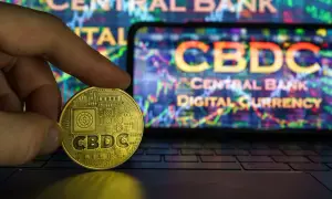 Złota moneta z napisem CBDC w dłoni na tle ekranu z wykresem i napisem "Central Bank Digital Currency". To przyszłość finansów, ale cbdc co to?