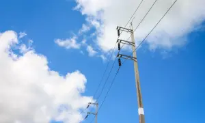 Słupy energetyczne na tle błękitnego nieba z chmurami. Widać przewody i izolatory. Określenie odległości słupa energetycznego od granicy działki jest kluczowe dla bezpieczeństwa.