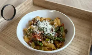 Makaron penne z zielonymi szparagami i suszonymi pomidorami, posypany parmezanem.