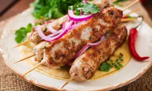 Aksamitny kebab z indyka na talerzu, ozdobiony krążkami czerwonej cebuli i świeżą natką pietruszki. Obok leży pikantna papryczka chili.