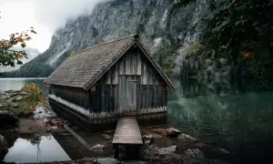 Alte Holzhütte am Ufer des Obersee-Sees, umgeben von steilen Felswänden und nebliger Atmosphäre.