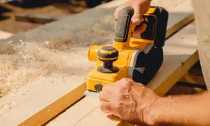 Un artisan utilise une raboteuse électrique pour raboter une porte en bois, produisant des copeaux fins.