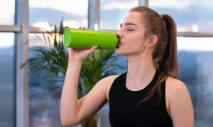 Junge Frau trinkt aus grüner Flasche. Sie fragt sich, wie viel Elektrolyte am Tag sie braucht, um fit zu bleiben.