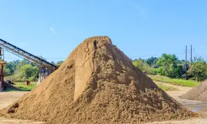 Ogromna hałda piasku na placu budowy, obok taśmociągu. Zastanawiasz się, ile kosztuje tona piasku?