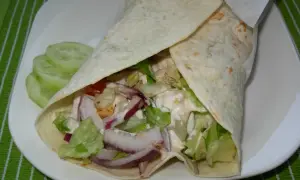 Pyszny domowy kebab w tortilli z kurczakiem, warzywami i sosem. Obok plastry ogórka.