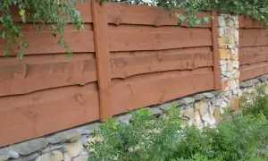 Solidne ogrodzenie z kamienia polnego i brązowych desek, otoczone zielenią.