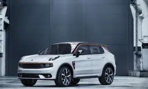 Biały Lynk & Co 01 z pomarańczowymi akcentami stoi przed szarą, industrialną ścianą.