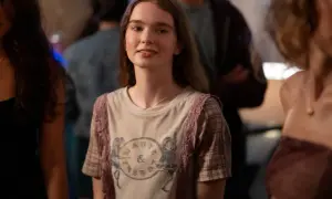 Młoda dziewczyna w koszulce z nadrukiem, przypominająca postać z filmów Chloë Grace Moretz, uśmiecha się na imprezie.