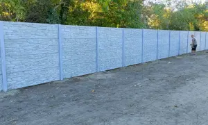 Mężczyzna z łopatą przy betonowym ogrodzeniu, zastanawia się, jak podwyższyć ogrodzenie betonowe, by zyskać więcej prywatności.