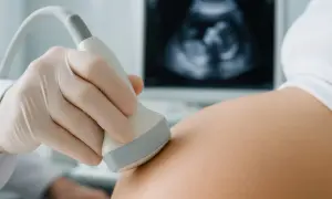 Pierwsze usg pierwszego trymestru. Dłoń w rękawiczce przykłada głowicę do brzucha, na ekranie widać obraz płodu.