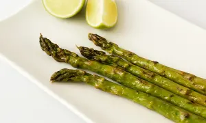 Asperges rôties sur une assiette blanche avec des quartiers de citron vert. Une idée simple pour une recette d'asperges savoureuse.