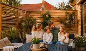 Familj njuter av kvällen på altanen, omgiven av ett vackert insynsskydd i trä.