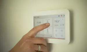 Dłoń dotyka ekranu termostatu, pokazując jak ustawić piec gazowy kondensacyjny ekonomicznie. Widoczna temperatura 19,5°C.