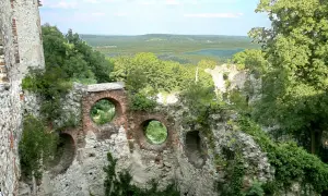 Ruiny zamku Tenczynek z okrągłymi oknami w ceglanym murze, otoczone zielenią i rozległym krajobrazem.