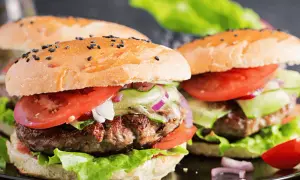 Dwa soczyste burgery z bułką posypaną czarnym sezamem, pomidorem, ogórkiem i sałatą.