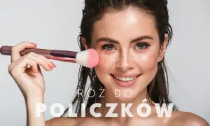 Uśmiechnięta kobieta nakłada róż na policzki puszystym pędzlem. Idealne miejsce, gdzie nałożyć róż, by podkreślić urodę.