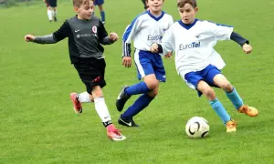Trzech chłopców w akcji na boisku piłkarskim. Wszyscy grają w piłkę nożną, pokazując zdrową rywalizację.