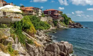 Skaliste wybrzeże z domami na klifie, restauracja z parasolami. Szukasz miejsca, gdzie nad morzem jest najtaniej?