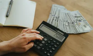 Ręka wpisuje kwotę na kalkulatorze obok stosu banknotów. Planowanie finansowe, jak zatrzymać odsetki u komornika, wymaga precyzji.