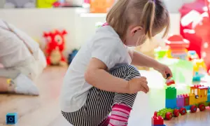 Niña de 0-3 años jugando con bloques de construcción. Crea un tren de juguete y una figura humana.