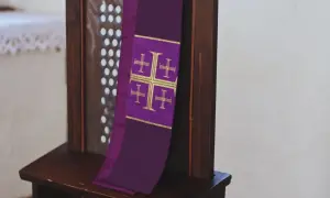 Fioletowa stuła z krzyżami, symbol sakramentu spowiedzi, wisi na drewnianej kratce konfesjonału.