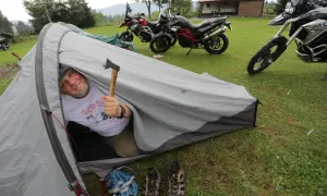 Mężczyzna w namiocie z siekierką, obok motocykle. Warto zabrać na wyprawę motocyklową namiot, buty i siekierkę.