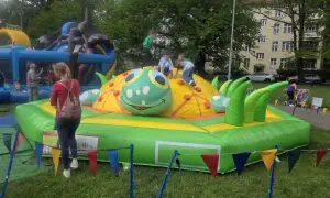 Dzieci bawią się na dmuchanej gąsienicy, która jest jedną z atrakcji dla 3 latka. W tle widać inne dmuchańce i budynek mieszkalny.