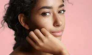 Portrait d'une jeune femme à la peau de couleur de peau olive, aux cheveux sombres et bouclés, posant sa main sur sa joue.