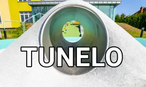 Tunel na placu zabaw z widokiem na kolorowe elementy i budynek.