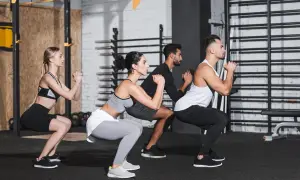 Uomini e donne eseguono squat a corpo libero in palestra, concentrati sull'esercizio.
