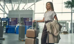 Kobieta z walizkami w poczekalni lotniska, gotowa do podróży samolotem. Na ramieniu ma narzuconą kurtkę.