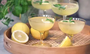 Fyra glas med gyllene limoncello, garnerade med citron och mynta. Perfekt för att lära sig hur dricker man limoncello en varm sommardag.