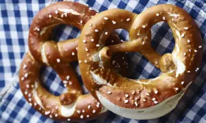 Zwei goldbraune Brezen mit grobem Salz liegen auf kariertem Stoff.