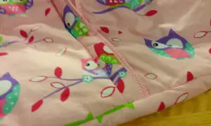 Różowy śpiworek niemowlęcy z kolorowym wzorem sów na gałęziach.