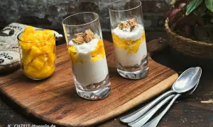 Zwei Gläser mit Mango-Creme und Kekskrümeln, daneben ein Glas mit Mangostücken. Perfekt für leichte ricotta rezepte.