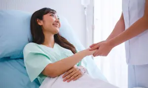 Una paciente sonríe mientras una enfermera le toma la mano, ofreciendo apoyo tras las contracciones después del parto.