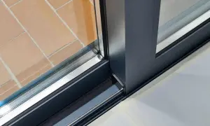 Detalle de perfil de ventana corredera con rotura de puente térmico, mostrando el interior y el exterior con baldosas de terracota.