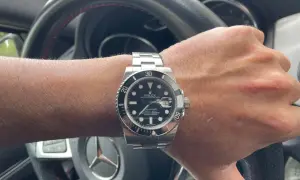 Mano con reloj Rolex Submariner, símbolo de invertir en relojes de lujo. El volante de un coche de alta gama sugiere un estilo de vida exitoso.