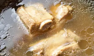 Gotujące się żeberka w bulionie, tworzące naturalną zupę mocy na stawy.
