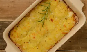 En ugnsform med gyllene, tunna potatisskivor, en klassisk pommes anna, toppad med en rosmarinkvist.