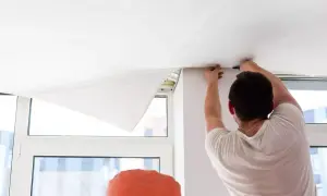 Montaż białego sufitu napinanego w łazience. Fachowiec precyzyjnie mocuje materiał do ramy.