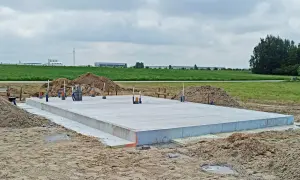 Solidna płyta fundamentowa na budowie, otoczona piaskiem i zielenią.