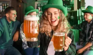Ragazza con cappello verde e trucco trifoglio offre due boccali di birra irlandese rossa in un pub festoso.