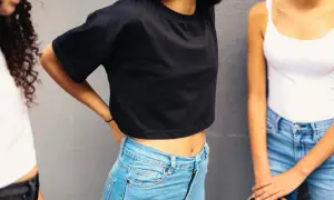 Trzy dziewczyny w bluzkach i jeansach na tle szarej ściany.
