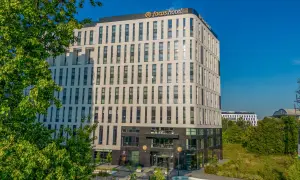 Nowoczesny budynek Focus Hotel Premium Warszawa z zielenią i błękitnym niebem. Idealne miejsce na pobyt.