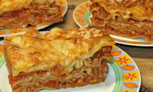 Prosty przepis na lasagne z mięsem mielonym. Pyszne, warstwowe danie z makaronem, sosem mięsnym i serem, podane na kolorowych talerzach.