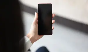 Dłoń trzyma telefon z czarnym ekranem, być może z powodu pogorszenia jakości zdjęć w telefonie.