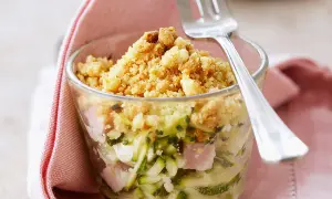 Un délicieux crumble de courgettes, jambon et fromage, servi dans un verre, prêt à être dégusté avec une fourchette.